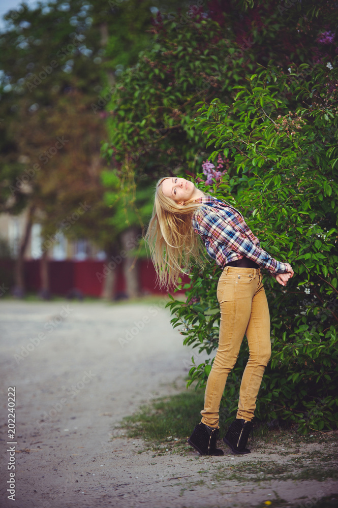 Fototapeta premium pretty woman blonde on a rustic road is happy, against a background of lots of green trees, a beautiful portrait of a rustic style, a simple home image