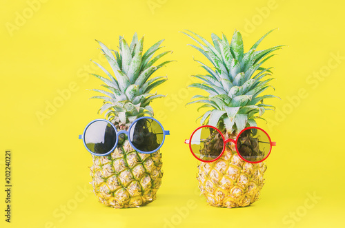 Pineapples with red and blue sunglasses on yellow background - Summer background