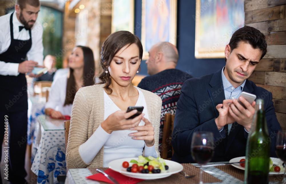 Portrait of man and woman in the restaurant with mobile phones