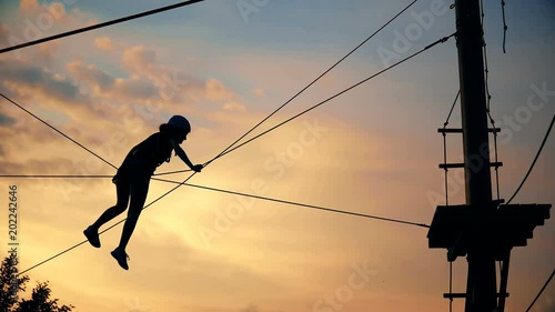 Young woman silhouette climbing in adventure park with friend summer free time at sunset vibrant sky photo