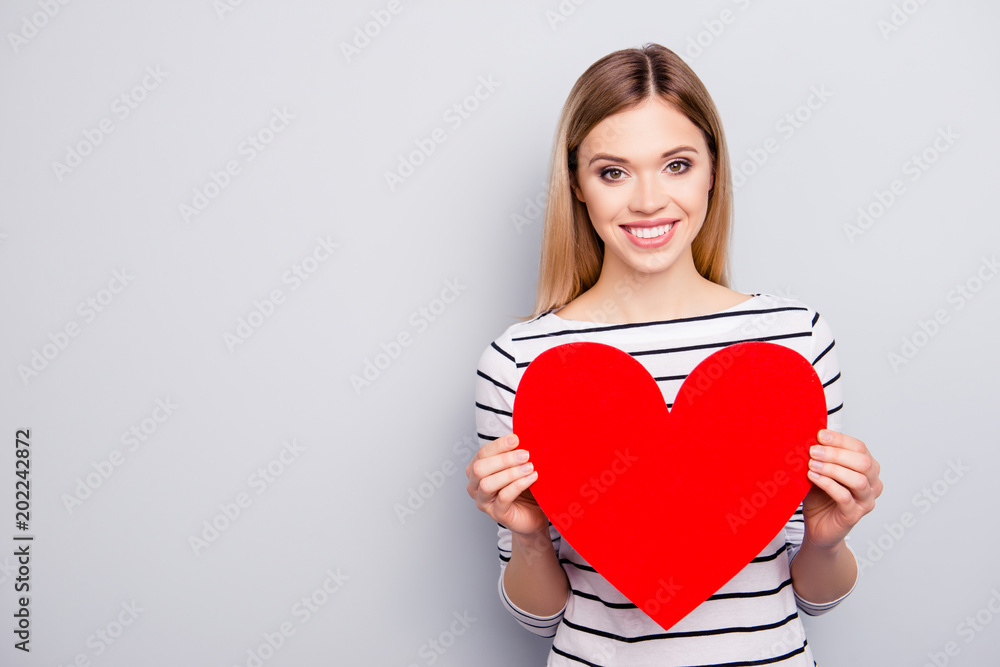 Portrait with copyspace, empty place for advertisement of attractive, charming, cheerful, cute, sweet girl with hairstyle having big red paper heart in arms isolated on grey background Portrait with copyspace, empty place for advertisement of attractive, charming, cheerful, cute, sweet girl with hairstyle having big red paper heart in arms isolated on grey background