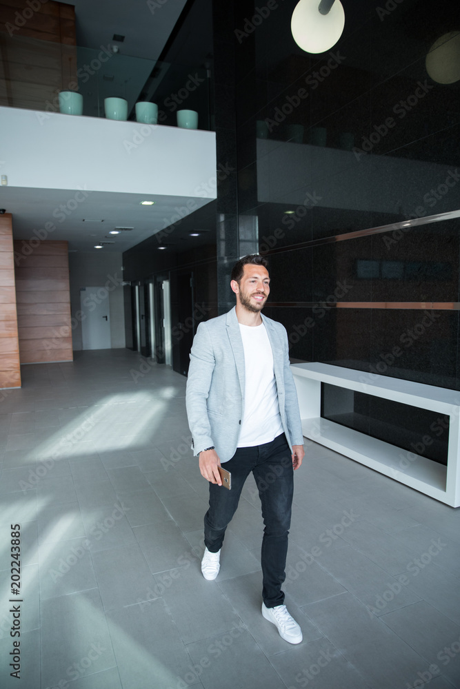 smiling young businessman leaving the nice office building with his smartphone after his work day. business concept smiling young businessman leaving the nice office building with his smartphone after his work day. business concept