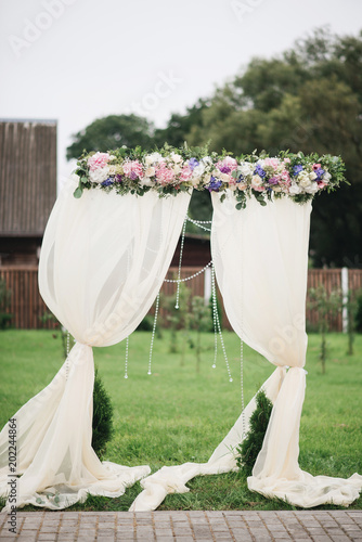 Obraz na płótnie Wedding arch decorated with cloth and flowers outdoors. Beautiful wedding set up. Wedding ceremony on green lawn in the garden. Part of the festive decor, floral arrangement. w salonie