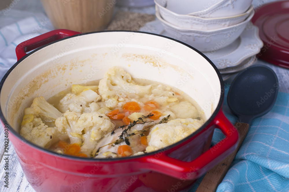 Cauliflower cooked in a red cast iron. A blue towel. Free space for text. Family dinner. Vegetables. Ready-made dish Cauliflower cooked in a red cast iron. A blue towel. Free space for text. Family dinner. Vegetables. Ready-made dish