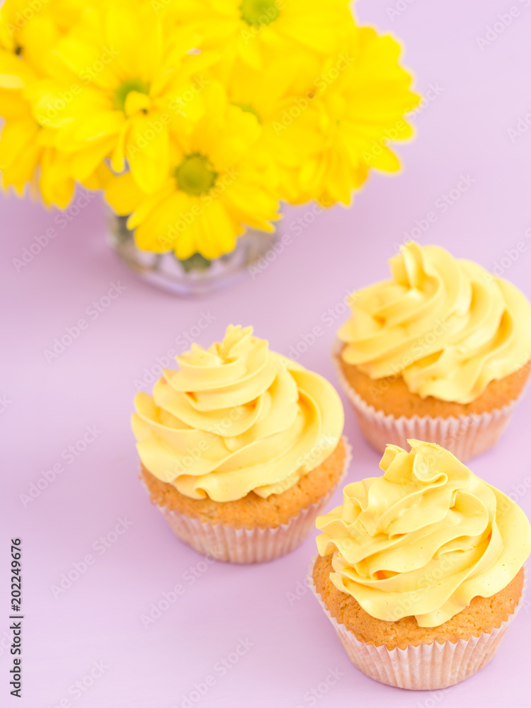 Cupcakes decorated with yellow cream and chrysanthemums on violet pastel background. Cupcakes decorated with yellow cream and chrysanthemums on violet pastel background.