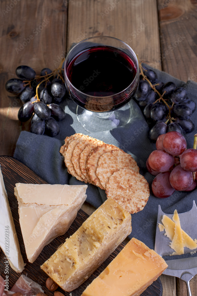 A glass of red wine and a snack. Grapes, cheese, biscuits, olives, ham. Italian food. Vertical photo. Uppertivo