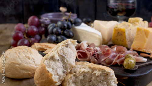 Italian appetizer of meat and cheese with fresh bread and wine. Wooden background