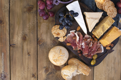 Snack to wine. Ham, different cheese, olives, grapes, bread and red wine in a glass. Wooden background. Itian food. Place for text. A party photo