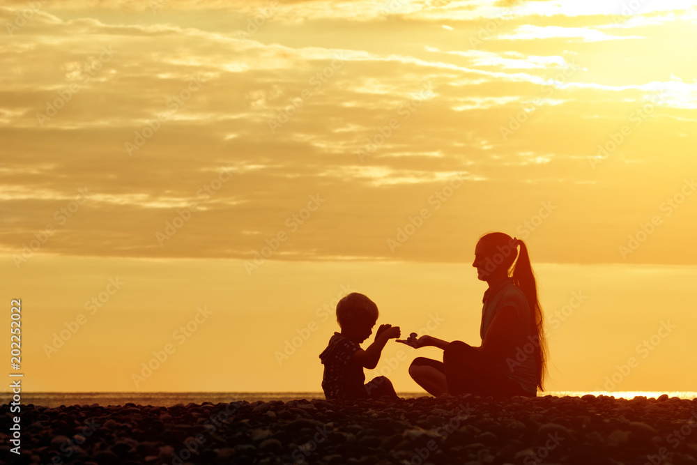 Mom and son playing on the beach with stones. Sunset time, silhouettes