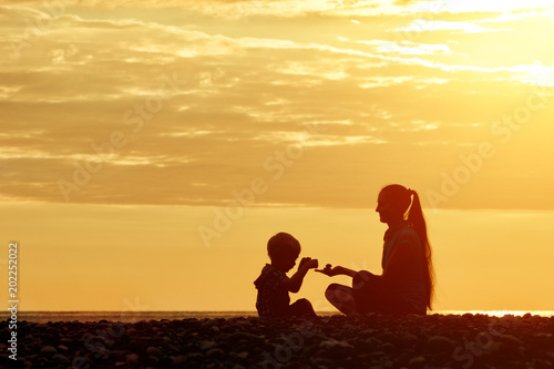 Mom and son playing on the beach with stones. Sunset time  silhouettes