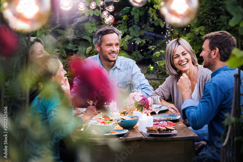Group of friends gathered around a table in a garden on a summer evening to shar Fototapet