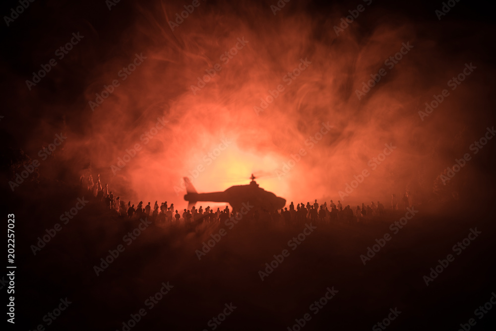 Military helicopter ready to fly from conflict zone or Silhouettes of a large crowd of people trying to escape with helicopter. Decorated night installed photo