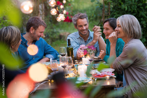 Wall Mural Beautiful summer evening in the garden, a group of friends in their forties have a good time laughing together around a table