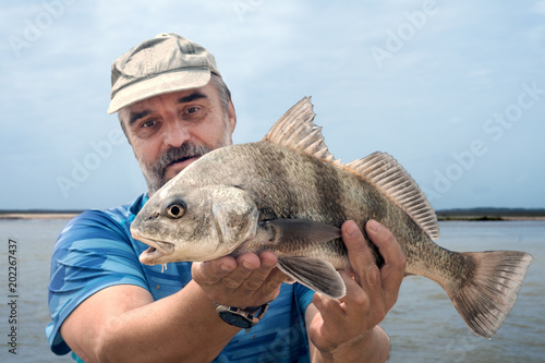 A fisherman is holding a fish  black drum (Pogonias cromis)  against the sea photo