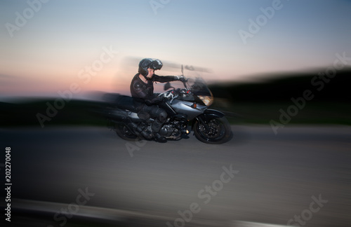 Fototapeta Naklejka Na Ścianę i Meble -  silhouette of rider on a motorbike driving at sunset with motion blur - space for your text