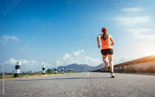 An asian woman athletic is jogging on the concrete road, she is warming her body and tideten her tying her shoes tightly fitting before workout.