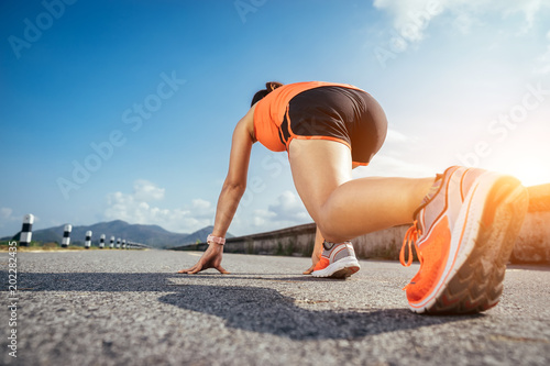 Fotografie An asian woman athletic is jogging on the concrete road, she is warming her body and tideten her tying her shoes tightly fitting before workout