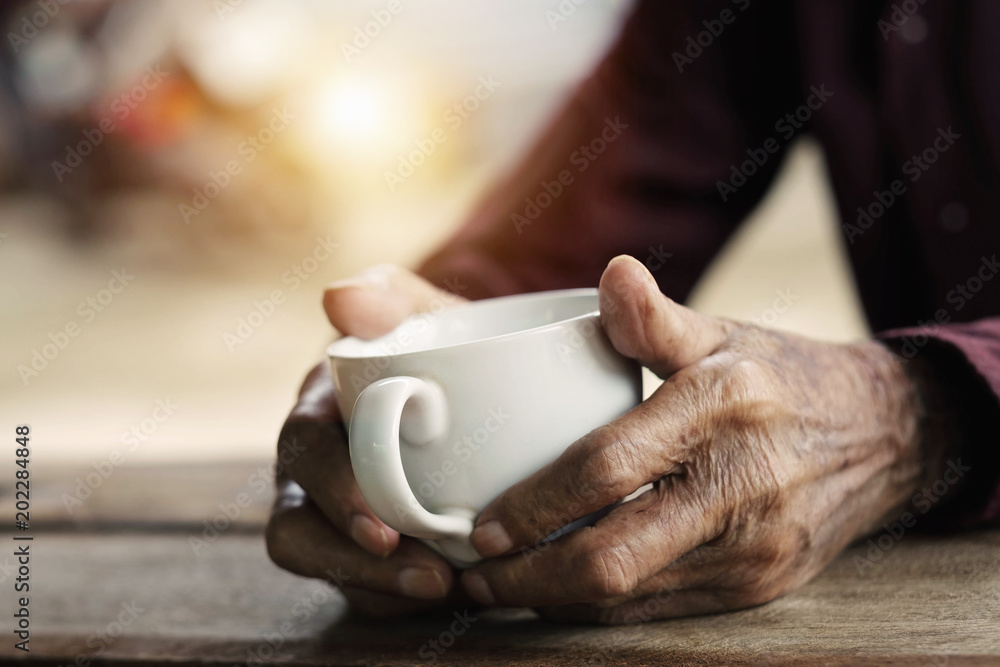 Hands of old man holding cup of coffee on the wood table.vintage tone
Hands of old man holding cup of coffee on the wood table.vintage tone