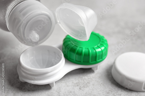 Dripping solution into contact lens case on light background, closeup