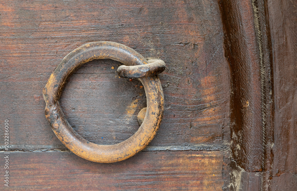 Closeup of rusted ring door knocker over an aged wooden door Closeup of rusted ring door knocker over an aged wooden door