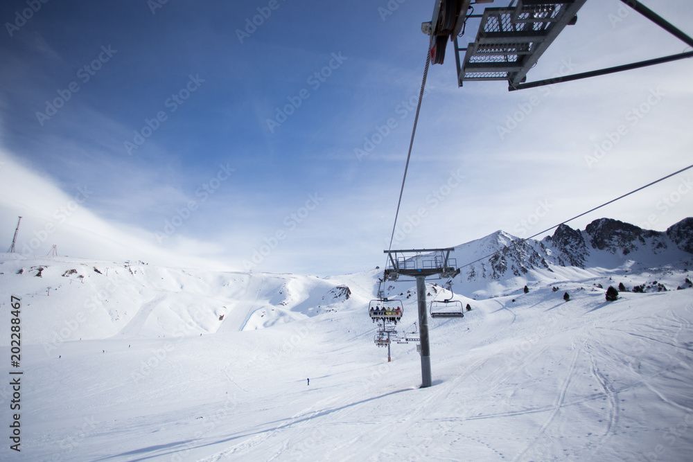View of ski and snowboard slopes landscape up in mountains winter sports resort, ski lift machine transports skiers and snowboarders to top of mountain on clear sunny day, perfect for winter vacation