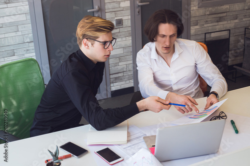 Photography Work harder! A couple of friends working together in business office, sitting beside the table and while using diagrams, talking about new planning project