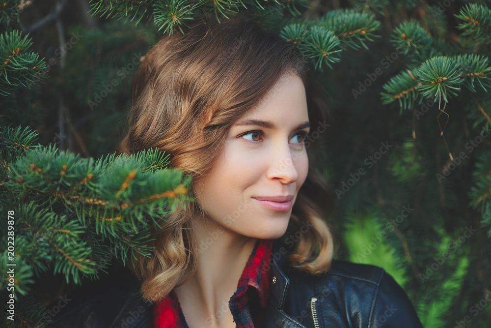 Beautiful face of a smiling young woman against a background of fir branches. Outdoor portrait in autumn park Beautiful face of a smiling young woman against a background of fir branches. Outdoor portrait in autumn park