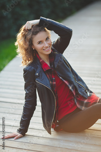 Beautiful young smiling woman in black leather jacket. Outdoor portrait in city park
