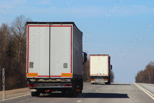 Transportation logistics - white semi trailer truck on asphalt road in summer on blue sky background, rear view