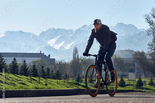 A man with the black bicycle goes against the background of big mountains in the city of Almaty