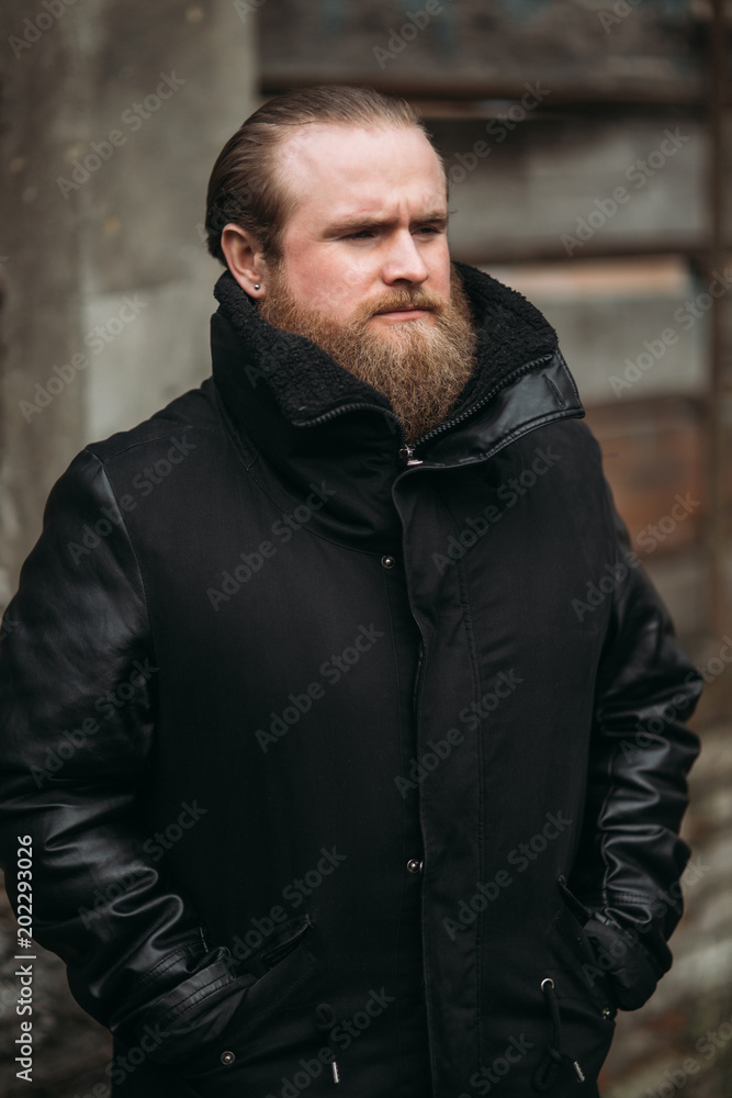 A bearded man in a black leather jacket stands outside and poses for a photographer A bearded man in a black leather jacket stands outside and poses for a photographer