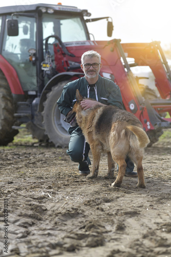 Farmer petting dog outside the barn, tractor in background