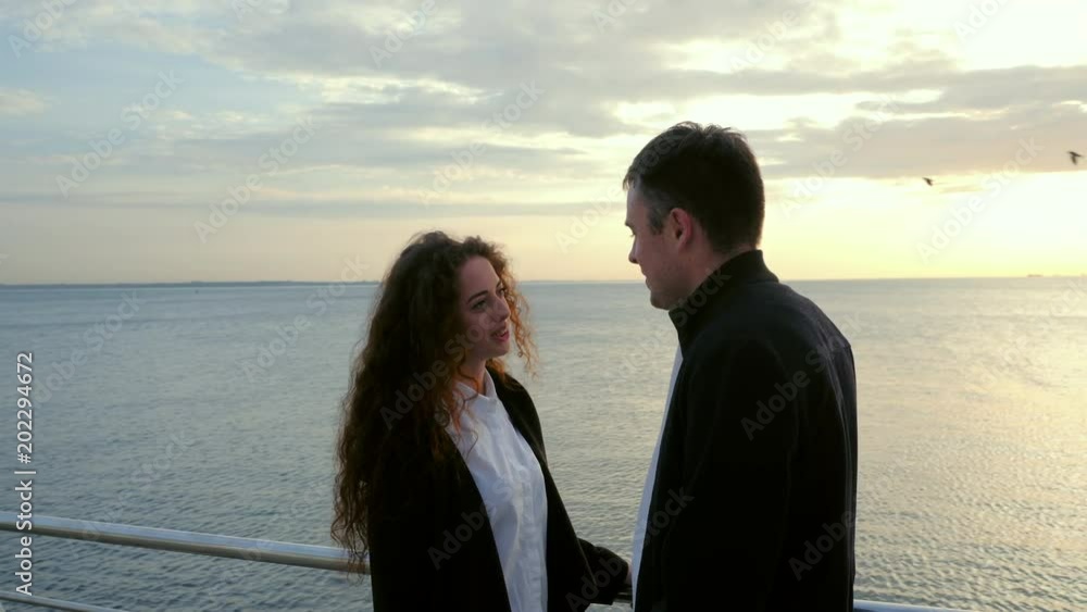 Young happy couple in love. Pair standing on wooden pier near sea or ocean and smiling to each other. People in black and white trendy clothing, They enjoying life. Romantic concept. 4k Young happy couple in love. Pair standing on wooden pier near sea or ocean and smiling to each other. People in black and white trendy clothing, They enjoying life. Romantic concept. 4k