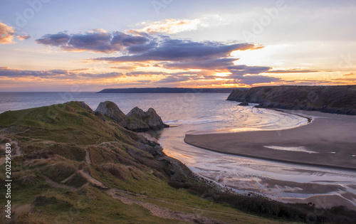landscape image of three cliffs bay at sunset with the tide in 