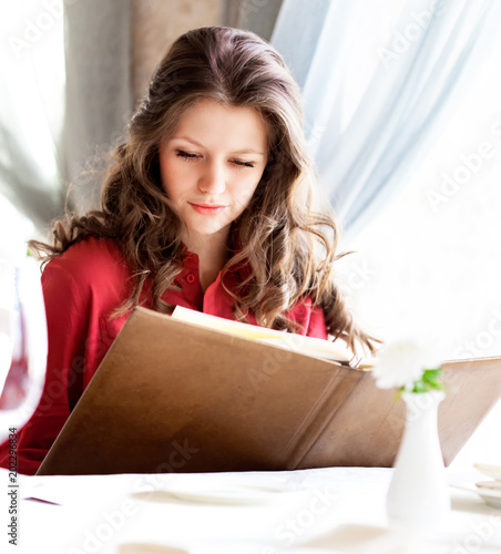 Cute beautiful woman in red at the restaurant. The girl is choising food in the menu. She is making an order photo