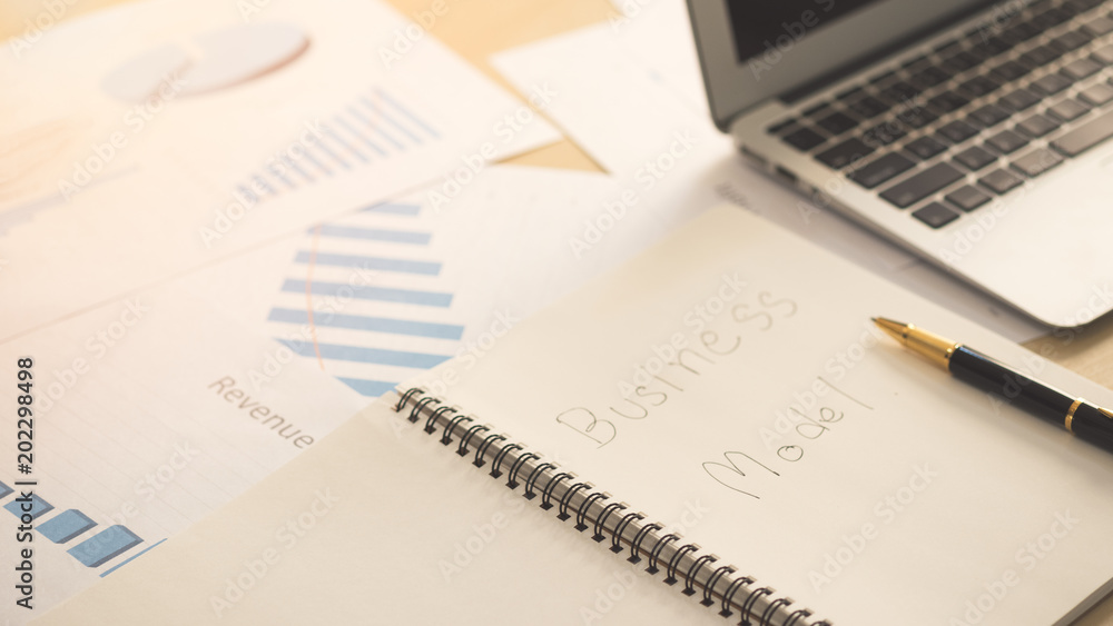 Opened notebook page with word business model on paper with blank screen laptop, pen and business documents on wooden table in office. Opened notebook page with word business model on paper with blank screen laptop, pen and business documents on wooden table in office.