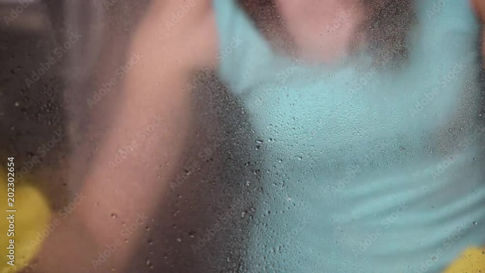A young woman washes windows in a house in yellow gloves using a spray with water and rags and sponges A young woman washes windows in a house in yellow gloves using a spray with water and rags and sponges