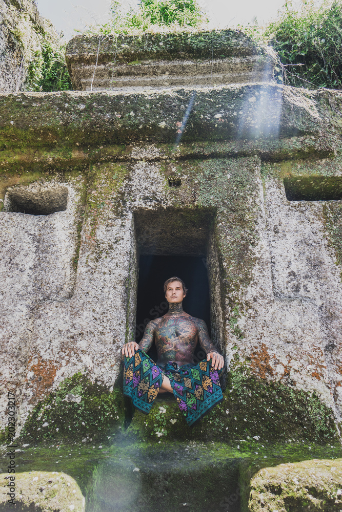 shirtless tattooed man sitting in ruins in bali, indonesia