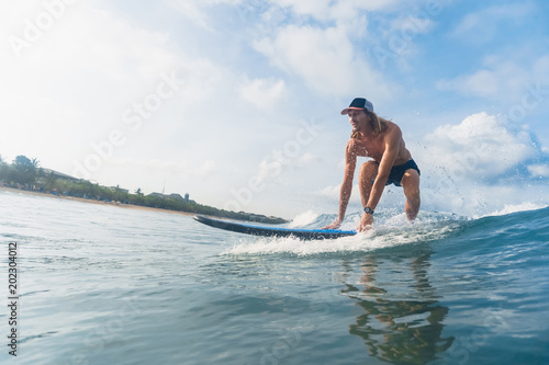 handsome man in swimming shorts and cap surfing in ocean © LIGHTFIELD STUDIOS