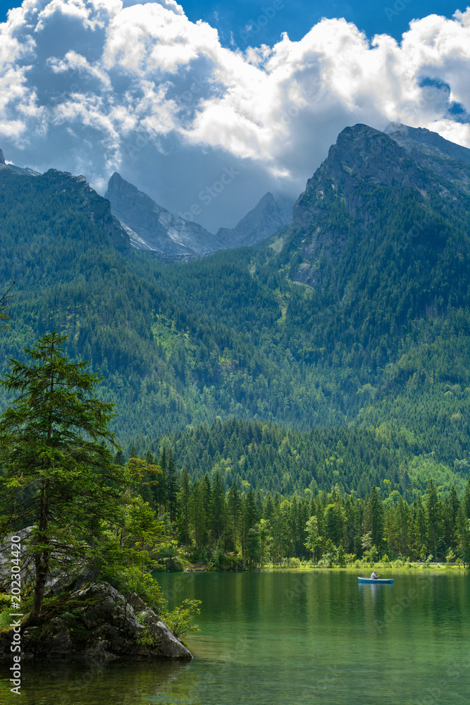 Lake against wooded mountains under big white cloud. Distant fisherman in boat