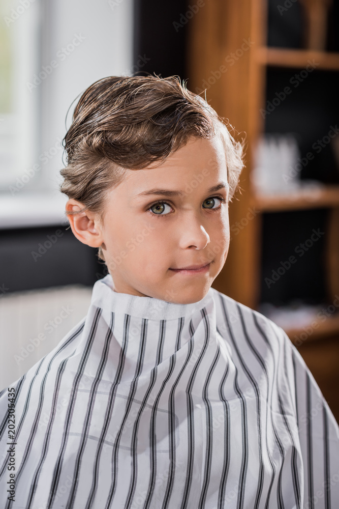 Fototapeta premium close-up shot of little kid covered with striped cloth at barbershop