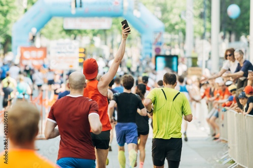 Mann macht freudig ein Foto beim Laufen mit Smartphone beim Marathon