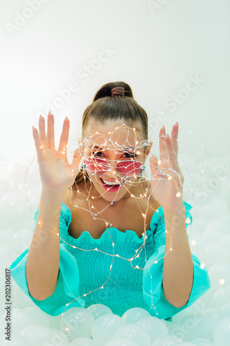 Happy beautiful woman lays surrounded by white plastic balls holding garland photo