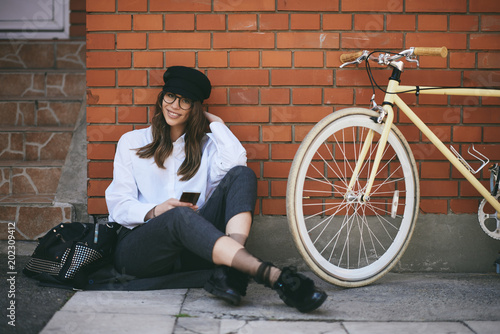 Woman sitting on sidewalk and using smart phone. Next to her yellow bicycle.