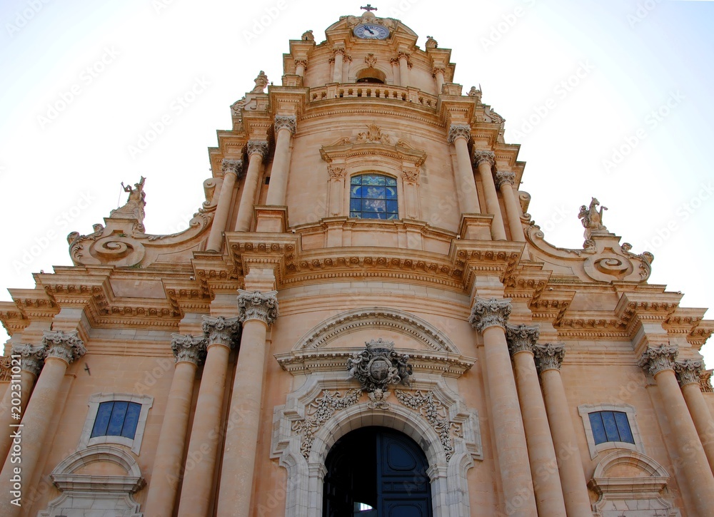 Façade of the baroque Duomo di San Giorgio or Cathedral of San Giorgio in Ragusa Ibla, Sicily, Italy, containing massive ornate columns, statues of saints and decorated portals 