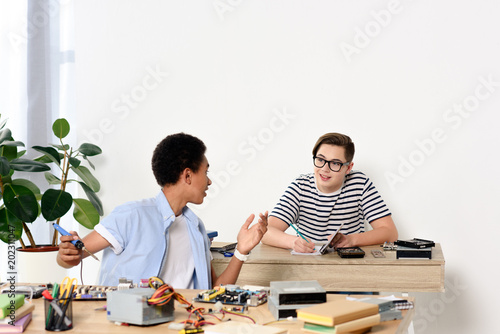 multicultural teenagers talking while fixing computer motherboard at home