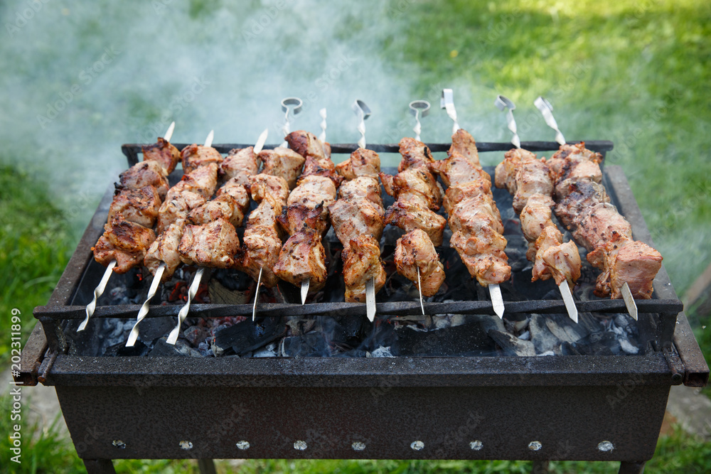 Shashlik or shashlyk preparing on a barbecue grill over Grilled cubes of pork meat on Outdoor. Stock Photo | Stock