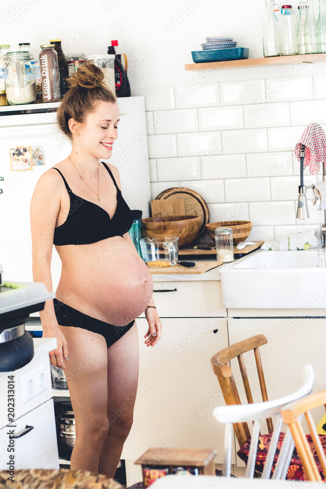 pregnant woman in underwear standing in her messy kitchen Stock Photo