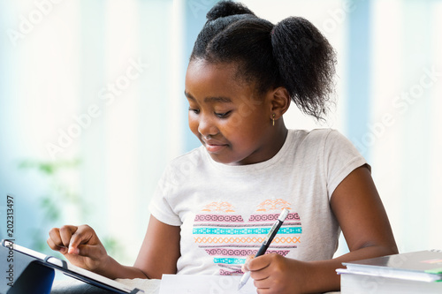 Cute african girl doing school work at home on digital tablet. photo