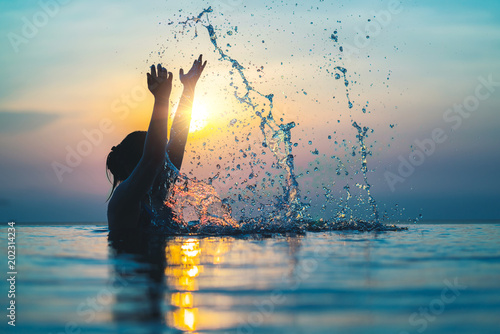 Black silhouette of asian woman splash water on summer vacation holiday relaxing in infinity swimming pool with blue sea sunset view. Healthy happiness lifestyle photo